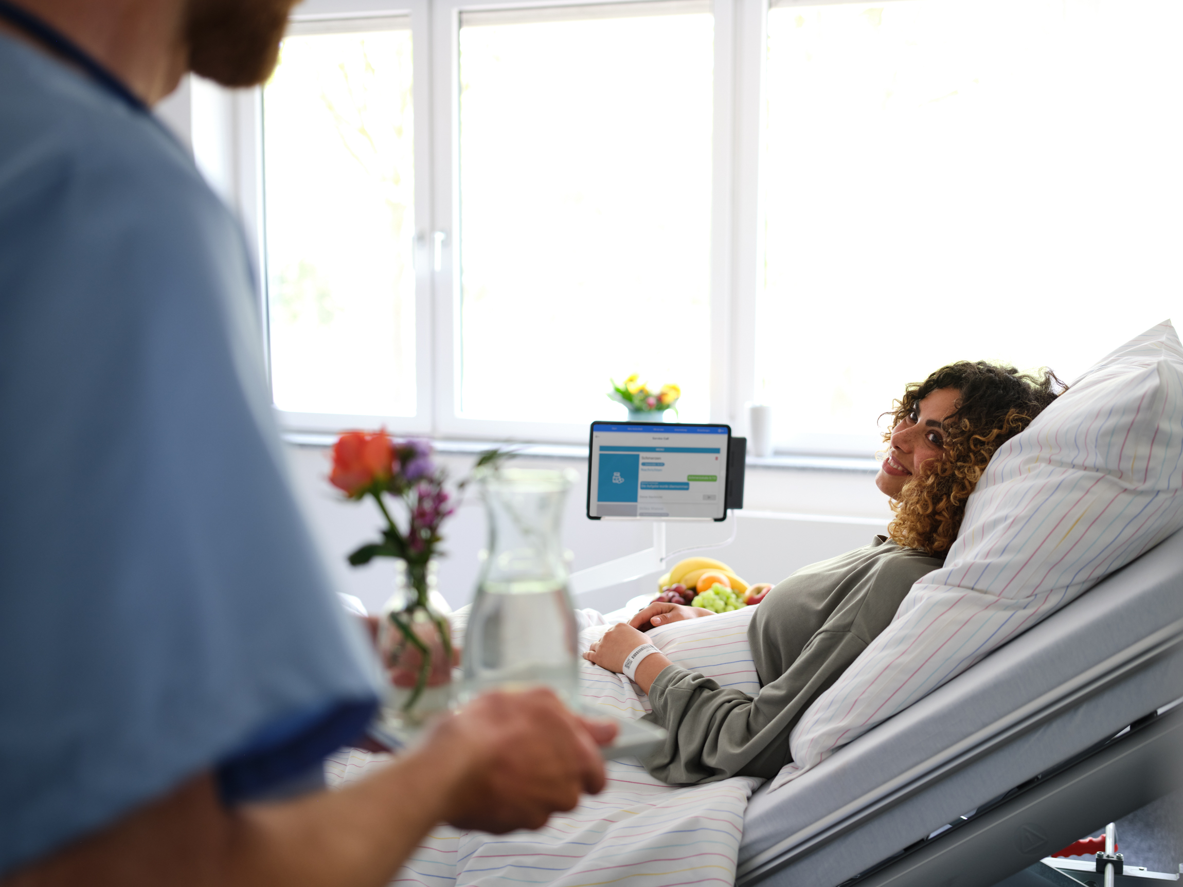 Patientenkommunikation: Pfleger bringt junger Patientin Wasser ans Bett, das sie über den Digitalen Serviceruf bestellt hat.