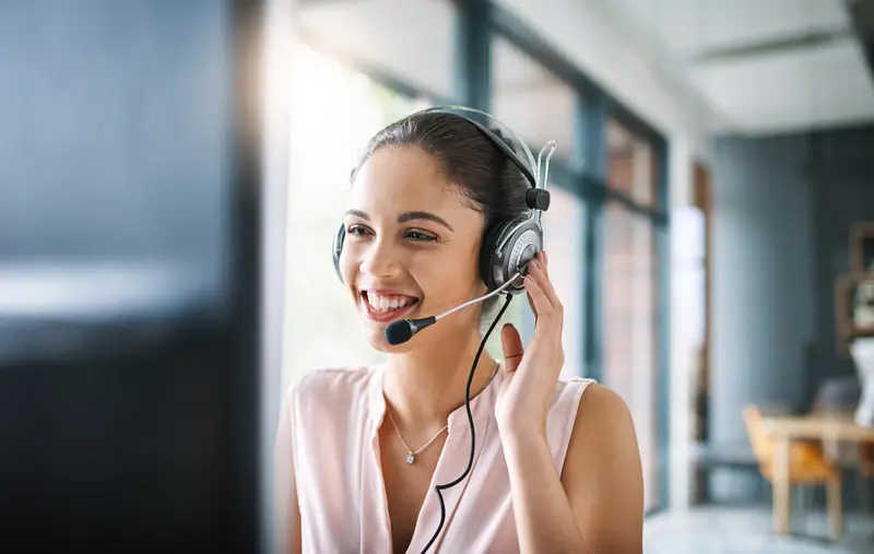 ConnectedCare Kontakt, junge Frau sitzt lächelnd am Computer und telefoniert über ein Headset