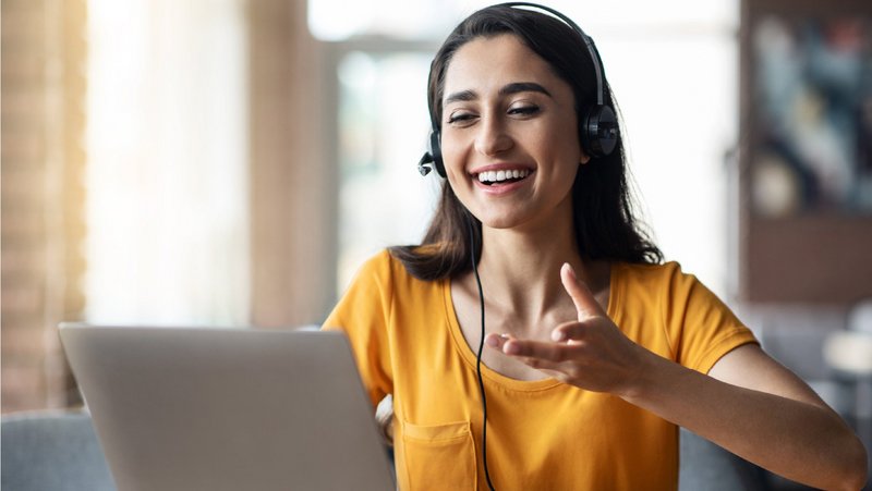 ConnectedCare Sales Partner | Frau mit Headset schaut lächelnd auf Laptop und gestikuliert mit den Händen
