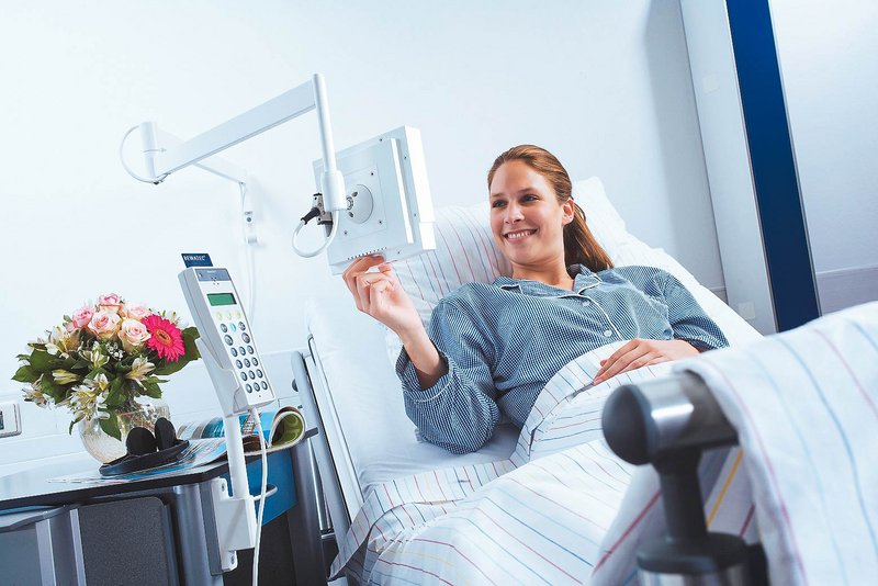ConnectedCare Unternehmensgeschichte | Patientin im Krankenhausbett bedient ConnectedCare MediTec LCD TV