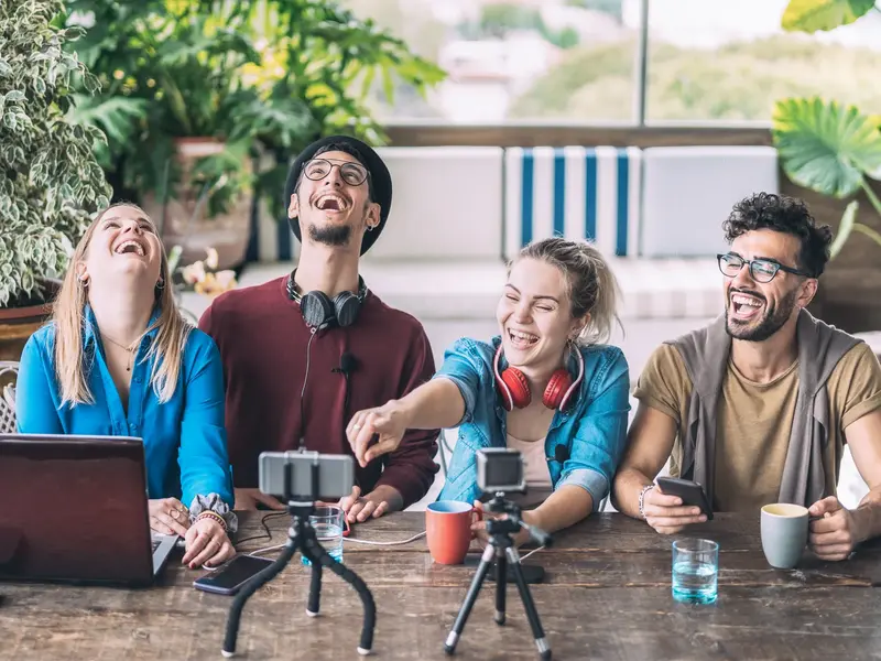 Vier junge Kolleg:innen teilen online kreative Inhalte mit Laptop, Smartphone und Co.