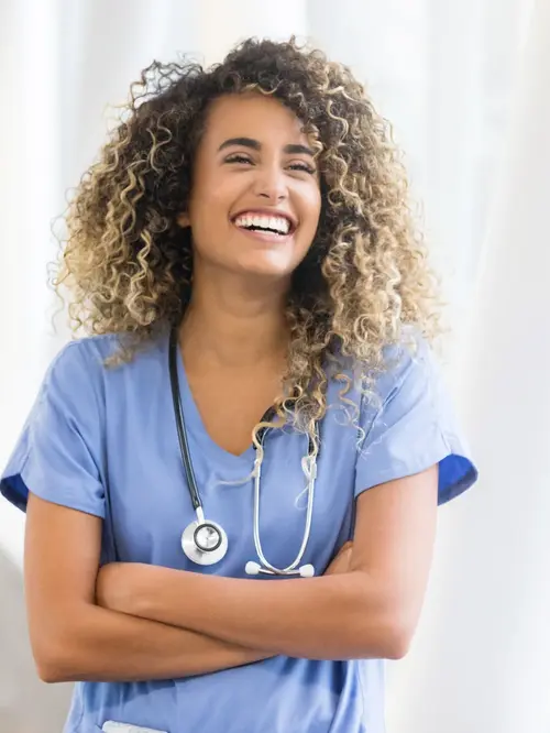 Junge selbstbewusste Pflegerin steht in einem Krankenhausflur und lacht herzlich. 