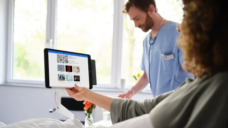 Krankenhaus digitalisieren: Patientin im Krankenhausbett bedient iPad mit eHealth Plattform ConnectedCare, ConnectedCare iPad-Halterung am Nachttisch